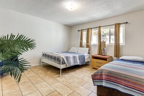 A bedroom with a bed, a bedside table, a lamp, curtains, and a potted plant.