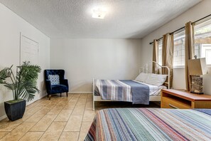 Quarto com cama, cadeira, planta em vaso e janela com cortinas.