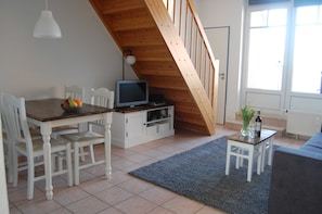 A dining area with a wooden table and chairs, a television on a cabinet, and a staircase leading to an upper level.