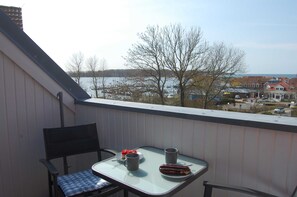 A balcony with a table, two chairs, and a view of a body of water and buildings.