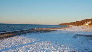 A beach with snow on the sand, a clear sky, and a distant shoreline. - Ferienwohnung Rerik - Ferienwohnung (Rerik)