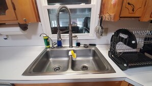 Una cocina con un lavamanos de acero inoxidable, una ventana arriba y un escurreplatos a la derecha.