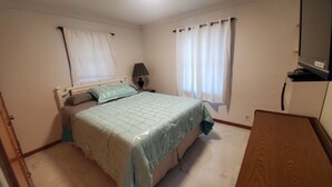 Un dormitorio con cama, mesita de noche, lámpara y ventana con cortinas.