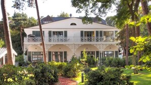 Um edifício de dois andares com varanda, rodeado por um jardim com um caminho.
