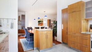 Cozinha moderna com armários de madeira, área de refeições com cadeiras e luminárias pendentes.