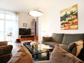 Ett vardagsrum med en soffa, ett soffbord i glas, en platt-TV och en tavla på väggen.
