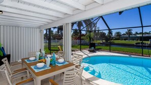 Un espace extérieur avec piscine, agrémenté d’une terrasse couverte, de chaises blanches et d’une table dressée pour les repas.