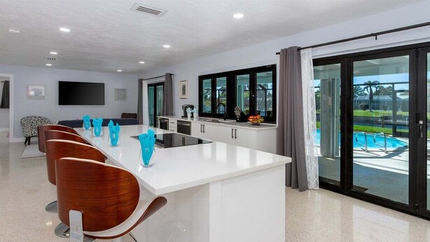 Une cuisine moderne dotée d’un îlot central, de tabourets de bar, d’un téléviseur à écran plat et offrant une vue sur une piscine.