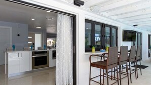 Une cuisine moderne avec des meubles blancs, un four en acier inoxydable et un coin repas agrémenté de chaises et d’une table en osier.