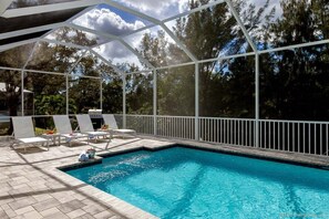 A pool area with a clear view of the sky and surrounding trees, enclosed by a white fence.