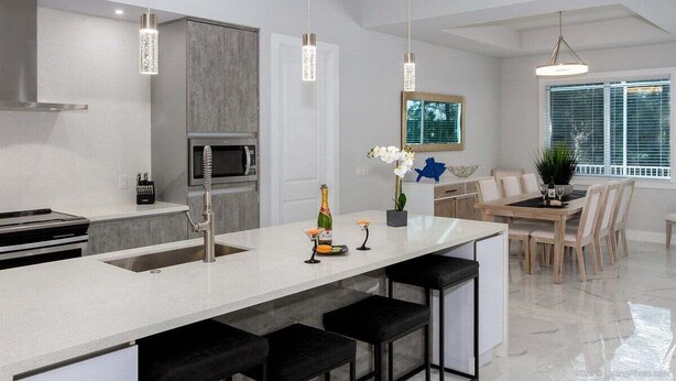 A modern kitchen with a central island, bar stools, pendant lighting, and a dining area with a view.