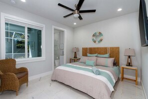 A bedroom with a bed, two bedside tables, a ceiling fan, a window, and a wicker chair.