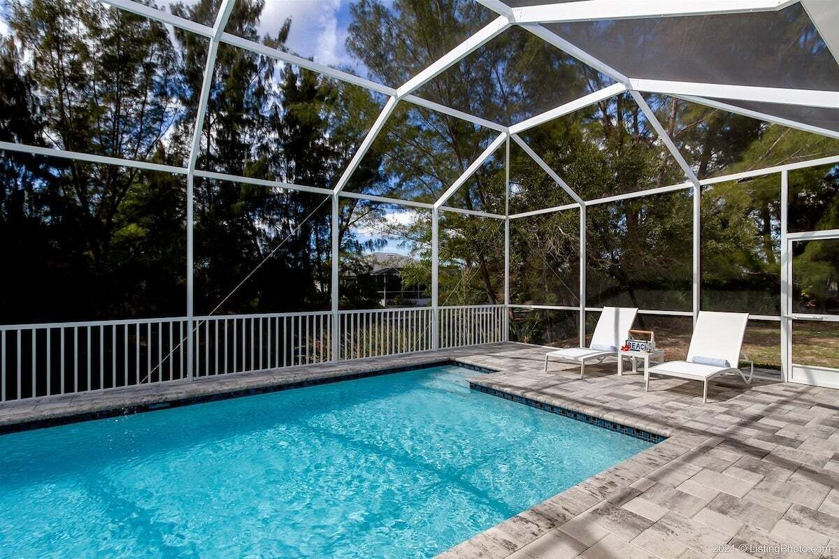A swimming pool with a covered area, surrounded by a white fence and trees.