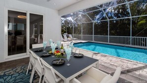 An outdoor dining area with a pool, white chairs, and a table set for a meal.
