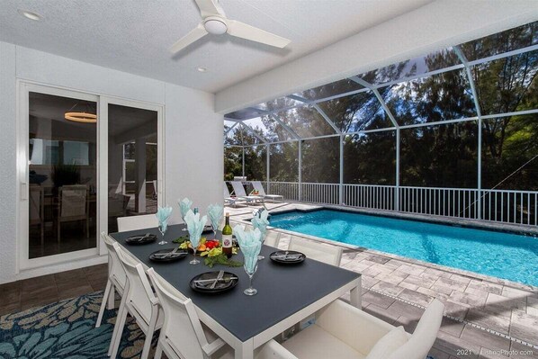 An outdoor dining area with a pool, white chairs, and a table set for a meal.