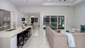 A modern kitchen with a central island, bar stools, pendant lighting, and a ceiling fan.