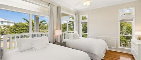 A hotel room with two beds, a ceiling fan, and large windows offering a view of palm trees.