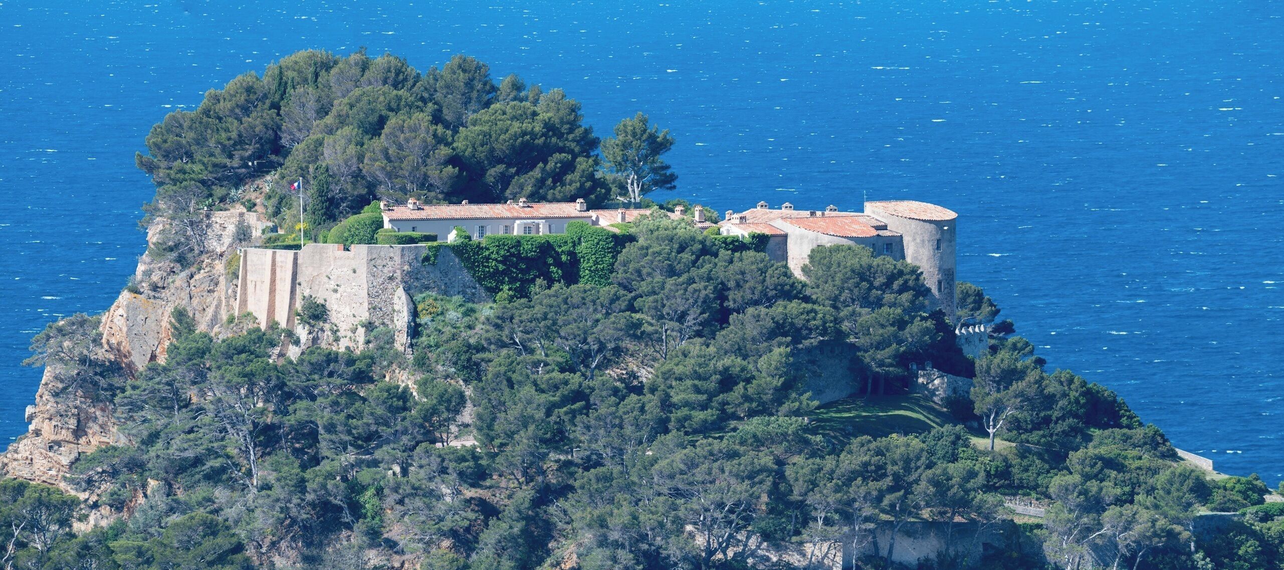 A coastal property with a castle-like structure, lush greenery, and a view of the sea.