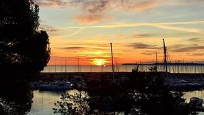 Ein Yachthafen mit vertäuten Booten, im Hintergrund ein Sonnenuntergang und im Vordergrund Bäume.