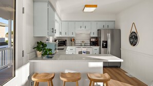 A kitchen with white cabinets, a large island with stools, a refrigerator, and a sign on the wall. - Canal Front Views, Boat Dock, Kayaks, 10" Walk to the Beach, Free Activities inc. Golf at Bear Trap. (Fenwick Island)