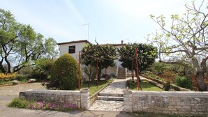 A stone pathway leading to a white building with a covered porch. - Apartment Paulinic (Rovinj)