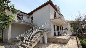 A two-story building with a stone-tiled patio, a staircase with white railings, and a balcony with a satellite dish. - Apartment Paulinic (Rovinj)