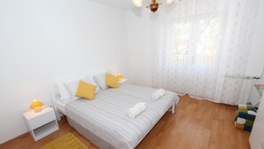 A bedroom with a bed, bedside tables, a lamp, a window with curtains, and a wooden floor. - Apartment Paulinic (Rovinj)
