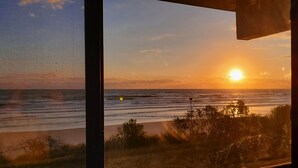 A sunset view through a window with a beach and ocean in the background. - 361 Fun in the Sun- Direct Oceanfront Ground Floor, 361 Fun in the Sun Summerhouse (Crescent Beach)