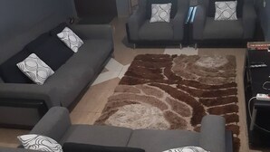 Ett vardagsrum med grå soffor, mönstrade kuddar, en brun och vit matta och en tv som står på ett TV-bord.