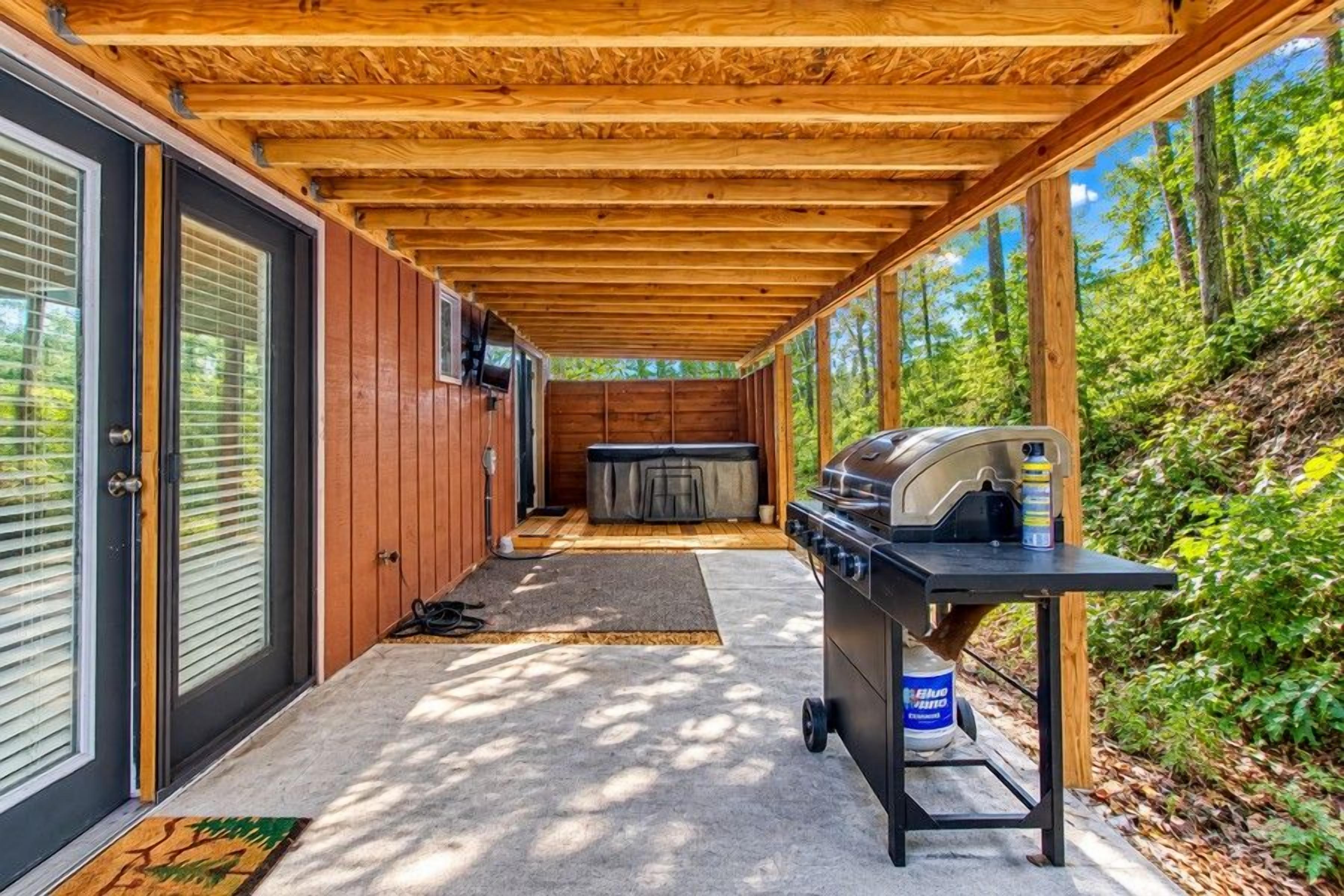 A covered outdoor area with a barbecue grill, a hot tub, and a door leading to a building.