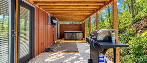 A covered outdoor area with a barbecue grill, a hot tub, and a door leading to a building.