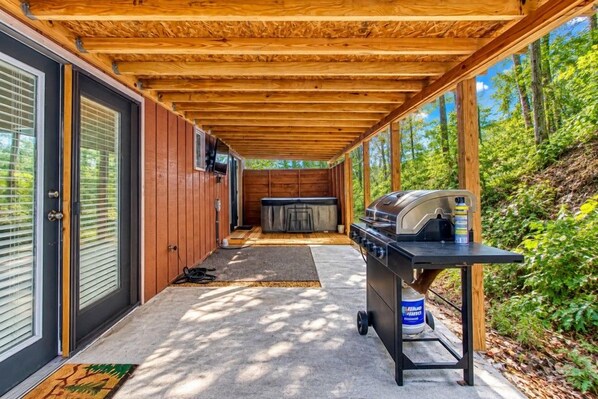 A covered outdoor area with a barbecue grill, a hot tub, and a door leading to a building. - Hidden Memories, Hot Tub, FREE Attraction tickets for each paid day, Pool Table! (Gatlinburg)