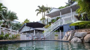 Uma área de piscina com cerca branca, espreguiçadeiras e escadaria que dá para uma varanda.