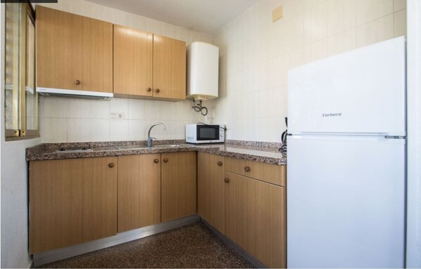 A compact kitchen with wooden cabinets, a white refrigerator, and a microwave on the countertop.