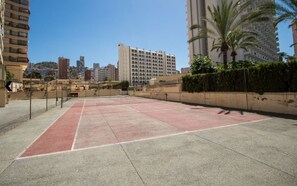 An outdoor tennis court surrounded by high-rise buildings, with a clear sky above. - AQUARIUM II 2-3 (benidorm)