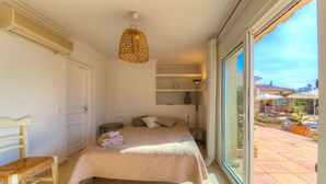 Quarto com cama, cadeira, mesa de cabeceira, abajur e vista para o pátio externo.