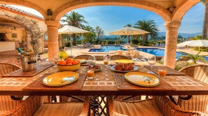A dining table set with plates, glasses, and a bottle, overlooking a pool and palm trees.