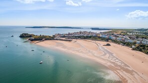 An aerial view of a coastal town with a sandy beach, a small island with a fort, and a densely built area with colorful buildings.