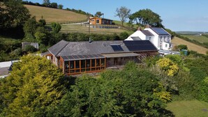 A large house with a glass conservatory, surrounded by lush greenery and a hilly landscape. - Brofallen - A secluded retreat with breathtaking views (Laugharne (1.8miles W))