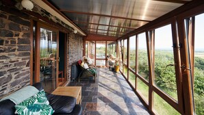 A covered patio with stone walls, a wooden table, and a sofa. - Brofallen - A secluded retreat with breathtaking views (Laugharne (1.8miles W))