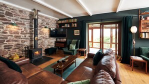 A cozy living room with a stone wall, leather sofas, a fireplace, and a bookshelf. - Brofallen - A secluded retreat with breathtaking views (Laugharne (1.8miles W))