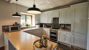 A modern kitchen with white cabinets, a large island, a microwave, a sink, and a stove. - Brofallen - A secluded retreat with breathtaking views (Laugharne (1.8miles W))