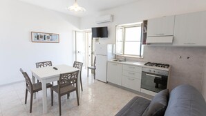 Une cuisine compacte comprenant une table à manger, des chaises, un canapé et un téléviseur fixé au mur.