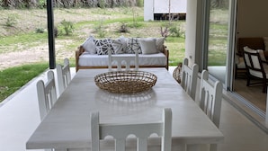 A modern dining area with a white table and chairs, a woven basket, and a view of a garden and building outside. - Fantastico Duplex Con Jardin y Piscina (Villa San Lorenzo)