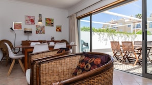 Un coin repas avec des meubles en osier, une table et des chaises, et une vue sur un bâtiment à travers une porte vitrée.