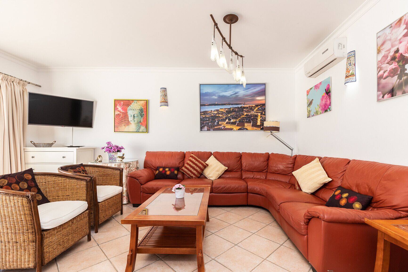 A living room with a sectional sofa, a TV, a flat-screen TV, wicker furniture, a coffee table, and wall art.