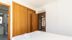 Une chambre d’hôtel avec une armoire en bois, un lit avec du linge de maison blanc et un climatiseur fixé au mur.