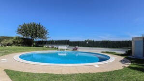 Una piscina circular con solárium empedrado, rodeada de un césped cuidado y un gran árbol.