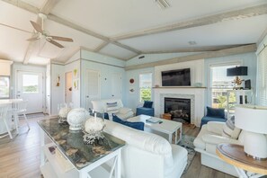 A spacious living room with a fireplace, white furniture, and a ceiling fan.