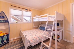 A child's bedroom with a bunk bed, a window with a view of a staircase, and a bookshelf with toys. - Beaulieu-Sur-Duck - Sanderling, Ocean View, Steps to Direct Boardwalk, Pets OK, Flex Stays (Duck)